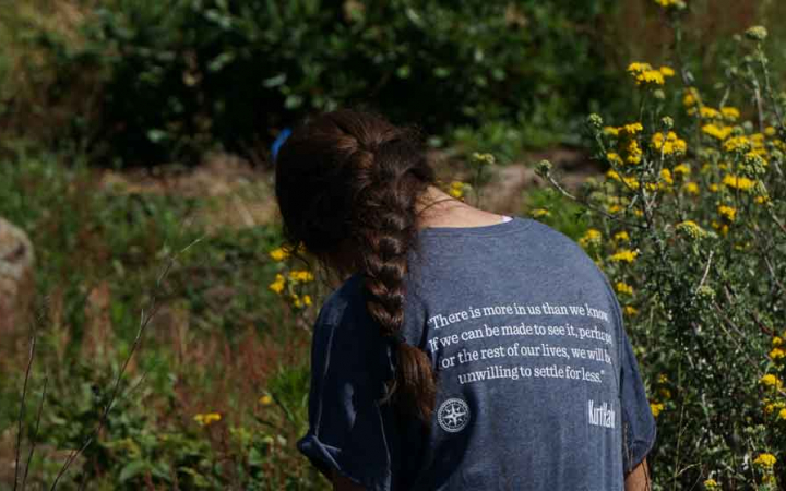 a person with their back to the camera sits among wildflowers, appearing to journal